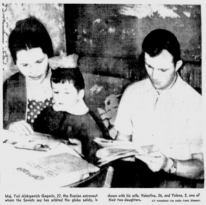 Black and white newspaper photo of Yuri Gagarin sitting at a table reading a newspaper next to his wife reading a book to their young daughter. Original caption: Maj. Yuri Aleksyevich Gagarin, 27, the Russian astronaut whom the Soviets say has orbited the globe safely, is shown with his wife, Valentina, 26, and Yelena, 2, one of their two daughters.