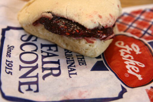 A tasty looking scone with raspberry jam filling, perfectly sized for eating in just a few bites, sitting on a red-and white bag right from the Fisher booth at the state fair.