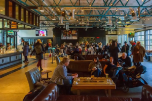 Seattleites sitting on couches and gathered around tables, many with coffee to drink, in a large open industrial-ish space with a coffee bar to one side across from large windows.