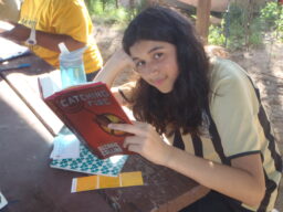 A teenager with long wavy brown hair sits at a picnic table reading Suzanne Collins's Catching Fire.