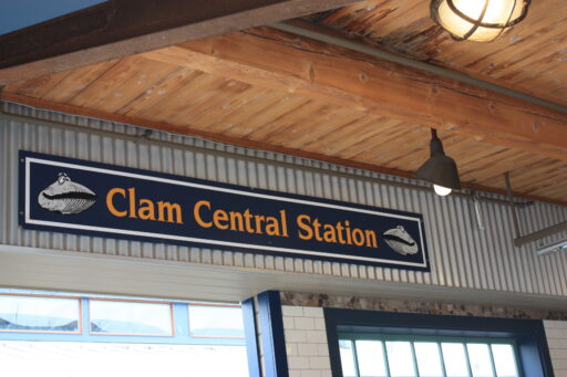 Inside Ivar's, a sign mounted near a wooden ceiling above windows says "Clam Central Station", with drawings of smiling clams with eyes on top of their shells.