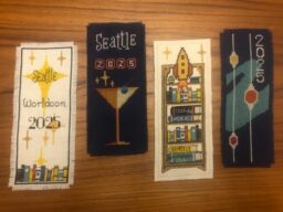 Four cross stitched bookmarks with various patterns representing Worldcon.