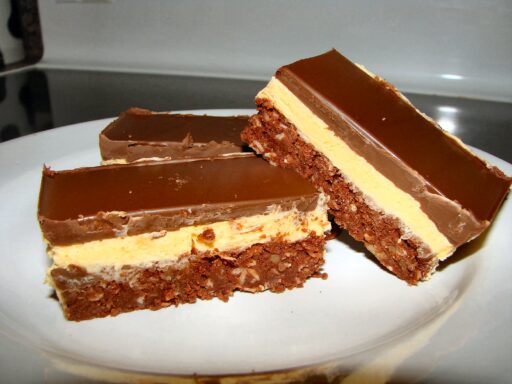 Three Nanaimo bars on a white plate; each is a three-layer treat of coconut crumb base, custard, and chocolate.