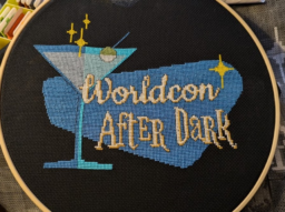 Text "Worldcon After Dark" over stylized martini glass in shades of blue, with yellow stars, cross-stitched in a round wooden frame.