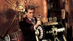 The hero of the film, dressed in suit, tie, and smoking jacket, sitting in the time machine, an ornately decorated device with a large round disk behind the chair, with springs and lights encased in cages, about to pull a lever topped with a large crystal knob.