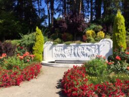 A carved low stone wall at the end of a path bordered by roses.