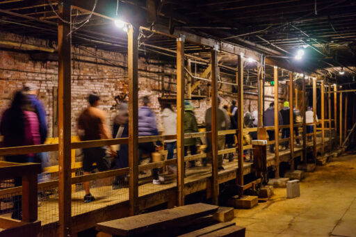 Tourists walk along a raised wooden walkway between a brick wall and a concrete floor in the Seattle underground.