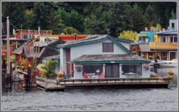 A grey two-story houseboat with teal and red trim and a front deck sits on the Seattle waterfront.