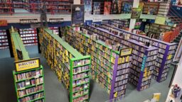 A view of Scarecrow Video's main floor as seen from the second floor, with green and purple shelves holding thousands of videos, with visible shelves sorted by director or country. Various movie posters and standees decorate the walls.
