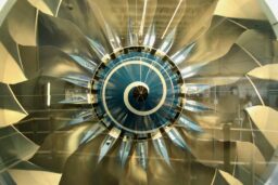 A jet engine fan seen from directly in front, with a white and blue spiral surrounded by silvery gold geometric fan blades.