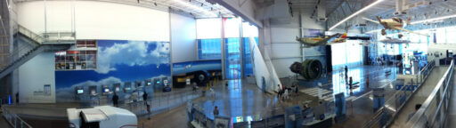 Panoramic view of part of the museum, showing displays, large jet engines, and aircraft hanging from the rafters.