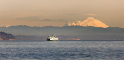 A ferry on the water in the distance at sunset, with Canada's Mt. Baker towering over the horizon.