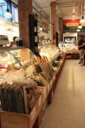 A grocery display case with wooden boxes full of baguettes in front of the case.
