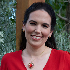 A portrait of a young, attractive, brunette woman smiling at the camera. She is wearing a red blouse and has a red, heart-shaped pendant.
