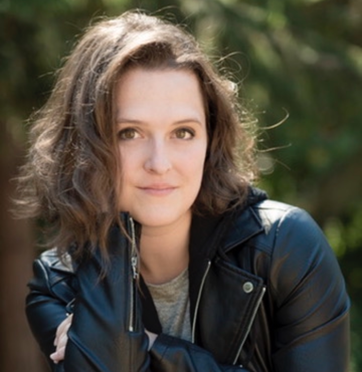 A brunette woman in a leather jacket smiles at the camera.