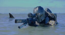 Still from Mando Mercs of an armored warrior rising from the ocean and holding a large rifle with a shark fin visible just behind them.
