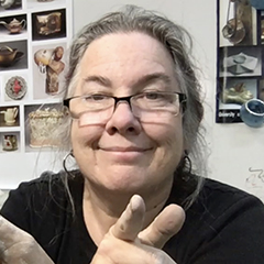 An informal headshot of the Snail Scott in her studio: a somewhat chubby white woman with long greying hair and reading glasses.