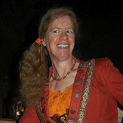 Head shot of a freckled woman with long red hair bound on the side of her head.